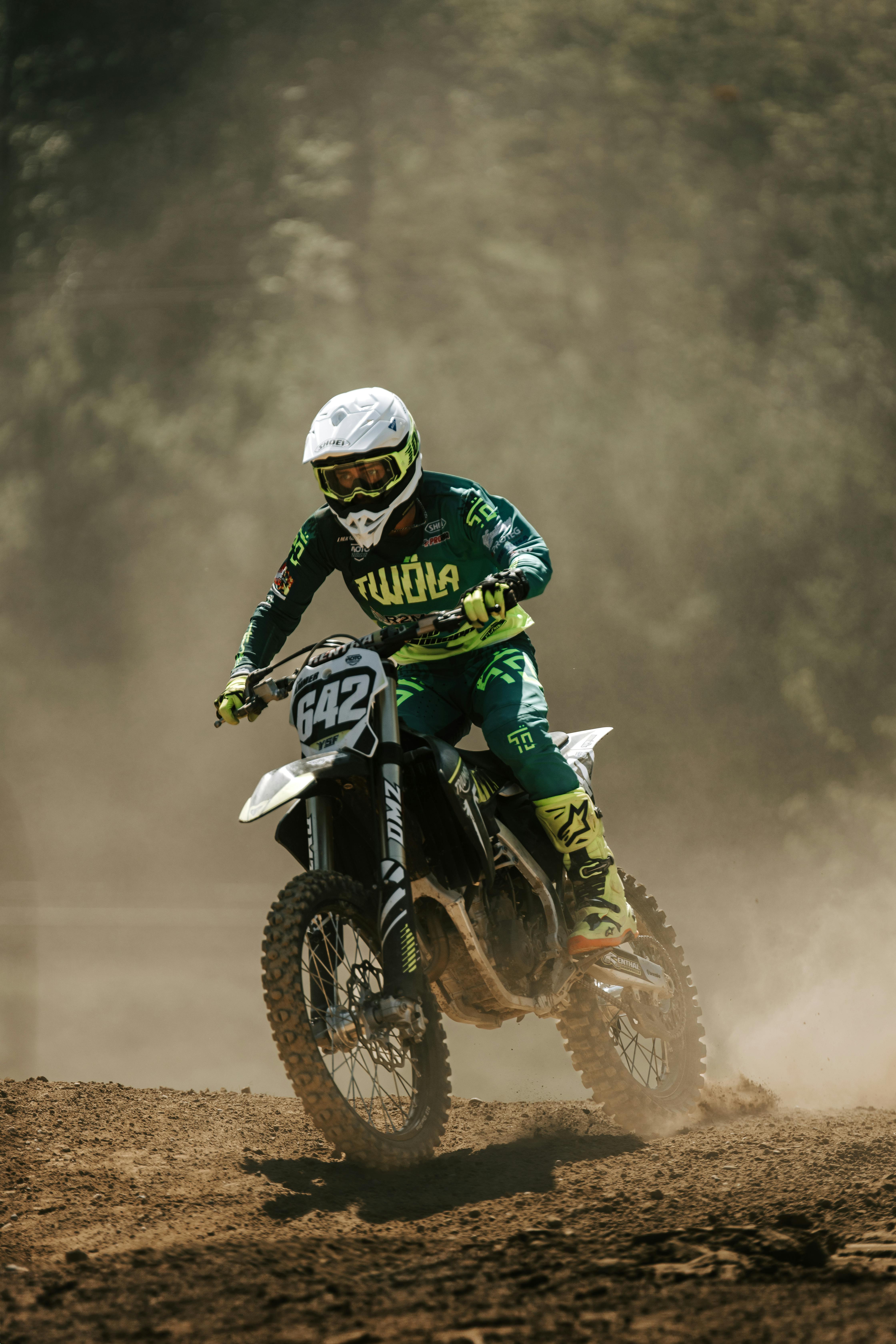 Motocross rider wearing custom gear racing on a dirt track, kicking up dust and exhibiting high energy.