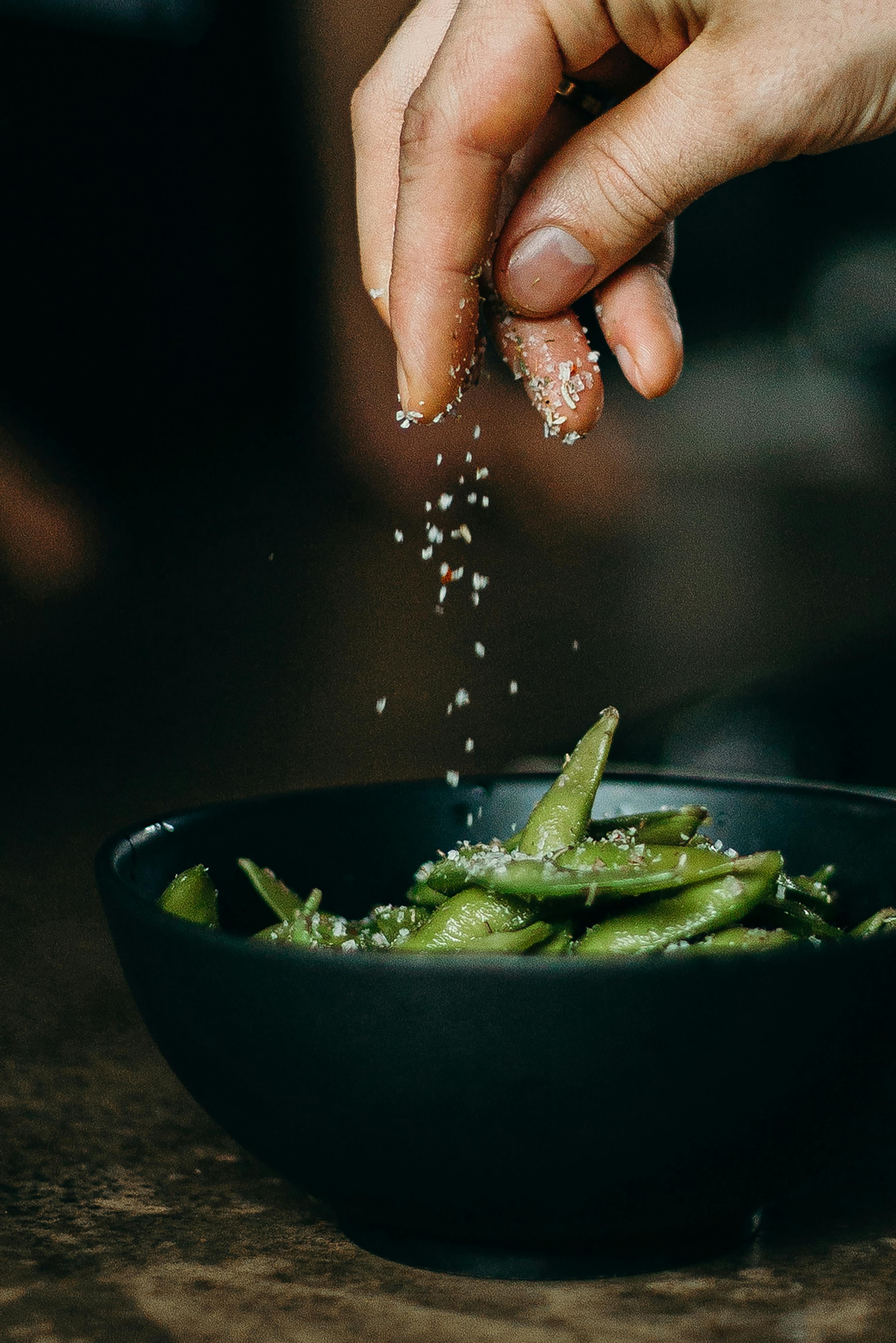 person pouring seasoning on green beans on bowl