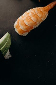 Delicious close-up of shrimp nigiri sushi with avocado on dark background, showcasing fresh ingredients.