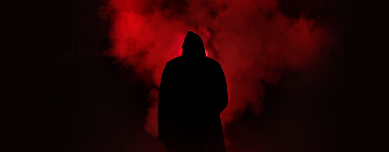 A mysterious silhouette standing against a backdrop of dramatic red smoke.