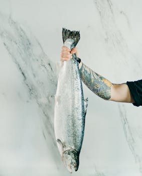 一条新鲜的鱼被放在大理石表面上的纹身手臂，展示了海鲜的新鲜度