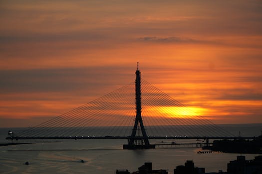 A beautiful sunset behind Tamsui River Bridge in New Taipei City, Taiwan, with warm orange hues.