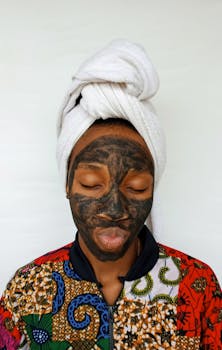 Young woman with clay mask and towel headwrap practicing skincare.
