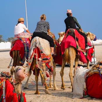 Three tourists on camels adorned with colorful blankets and nets in a desert setting.