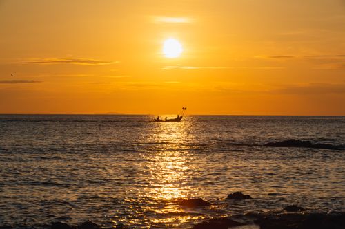 Free Silhouette of a fishing boat at sunset with golden sky reflecting on the ocean. Stock Photo