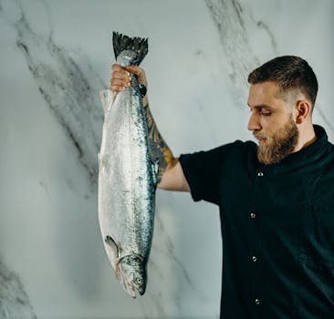 A chef holding a fresh salmon fish in a kitchen, ready for preparation.