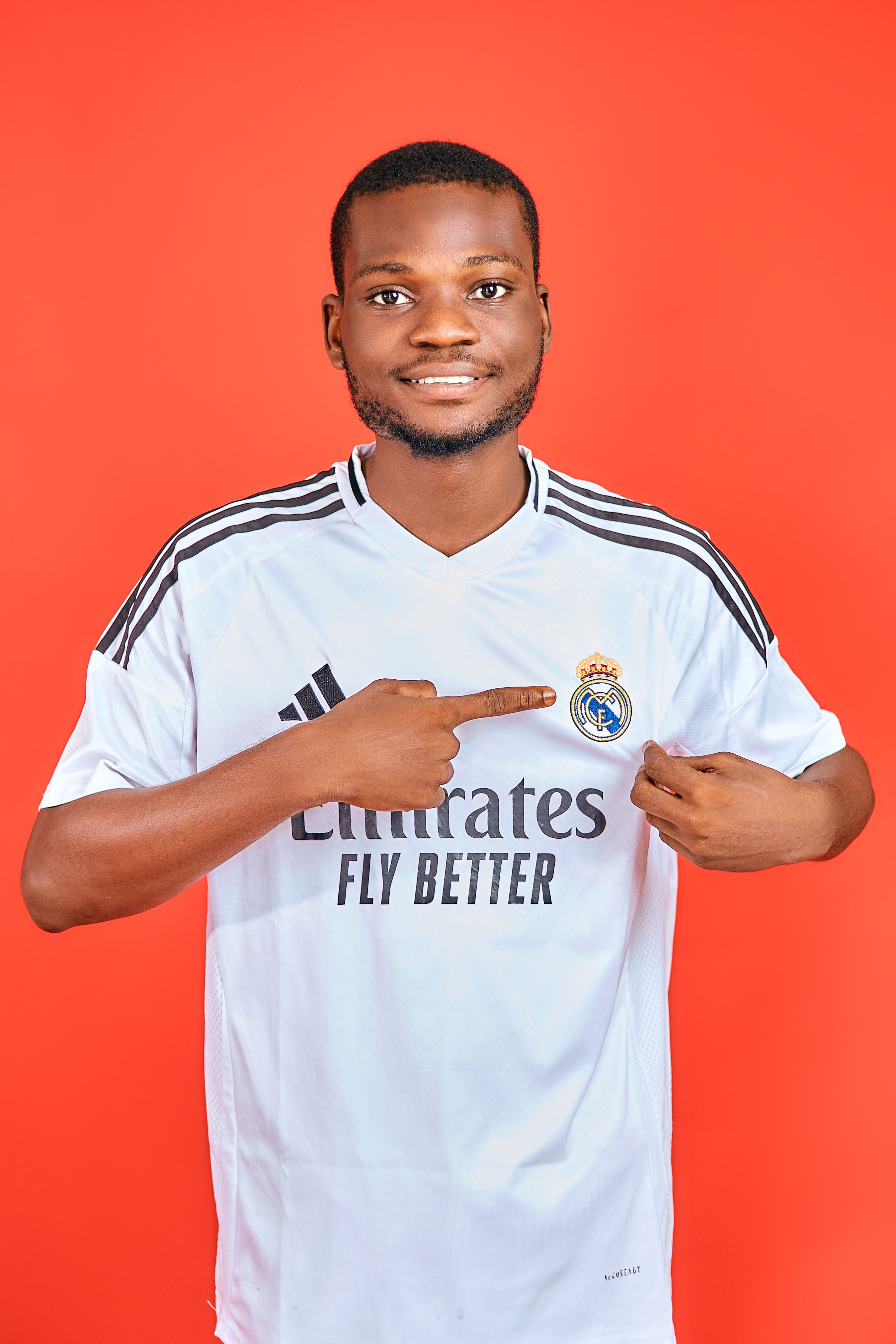 Young man in white soccer jersey pointing at logo on vibrant red background.