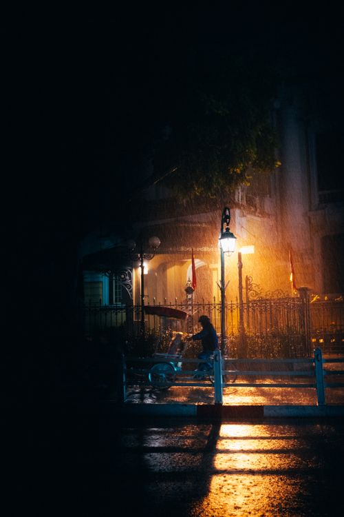 Free Captivating night scene of a cyclist under a streetlamp in rainy Hà Nội, Vietnam. Stock Photo