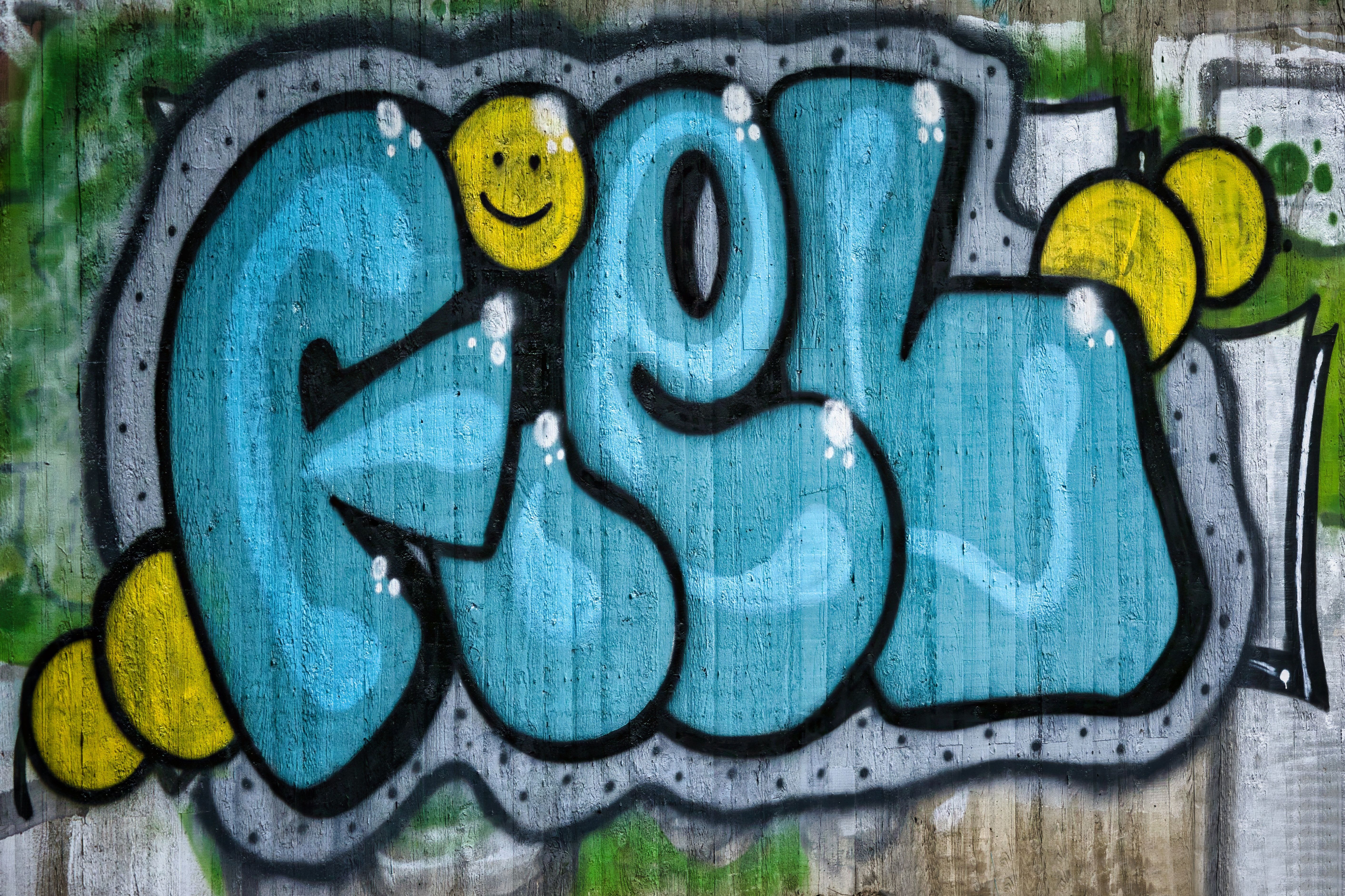 Colorful graffiti artwork with blue letters and a smiley face on a concrete wall.