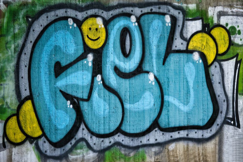 Colorful graffiti artwork with blue letters and a smiley face on a concrete wall.