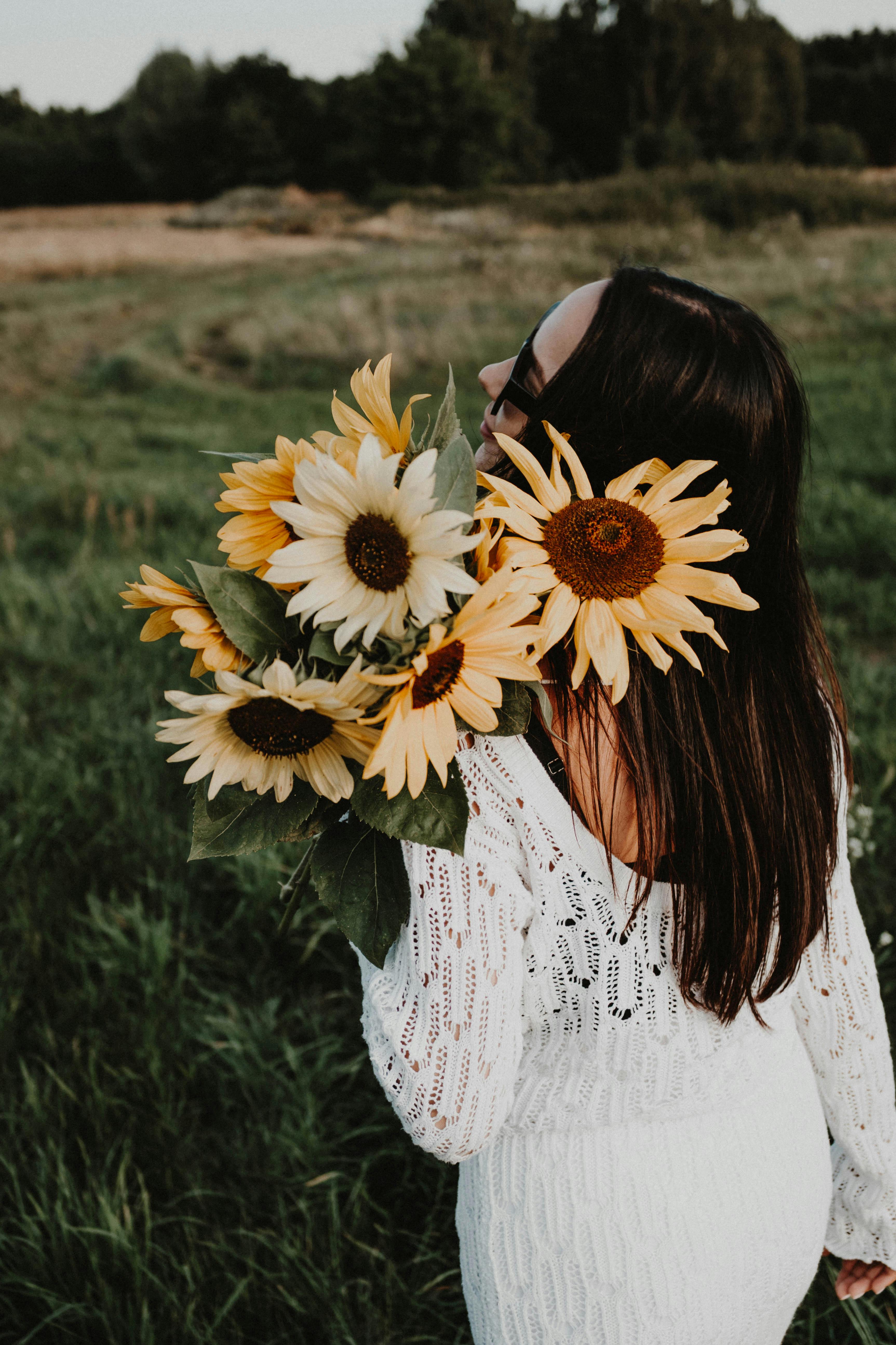 Woman in white lace dress embraces sunflowers in a sunny field.