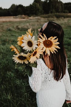 Woman in white lace dress embraces sunflowers in a sunny field.