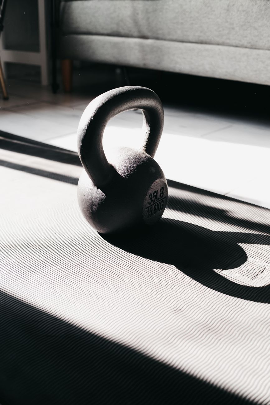 A kettlebell sitting on gym matting in bright light, the sort of simple storage-and-flooring setup that keeps garage gear usable