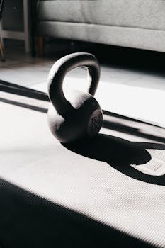 Kettlebell in bright sunlight casting shadow on gym mat indoors, perfect for fitness themes.