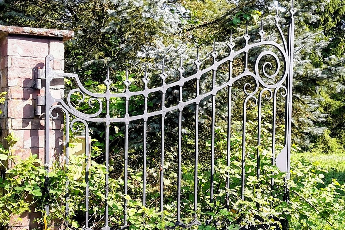 Poartă din fier forjat cu model decorativ lucrat, înconjurată de vegetație bogată