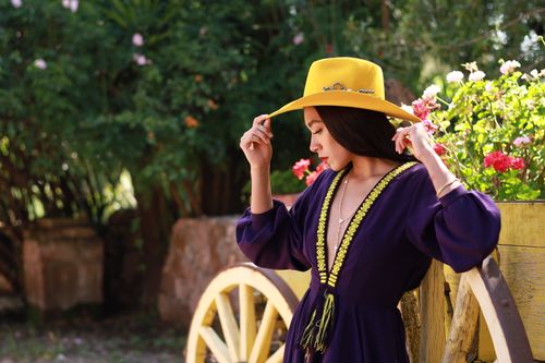Free Fashionable woman in a yellow hat poses in a lush garden with vibrant flowers and a wooden wheel. Stock Photo