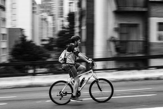 Dynamic black and white shot of a cyclist in mid-motion on a city street, emphasizing speed and urban life.