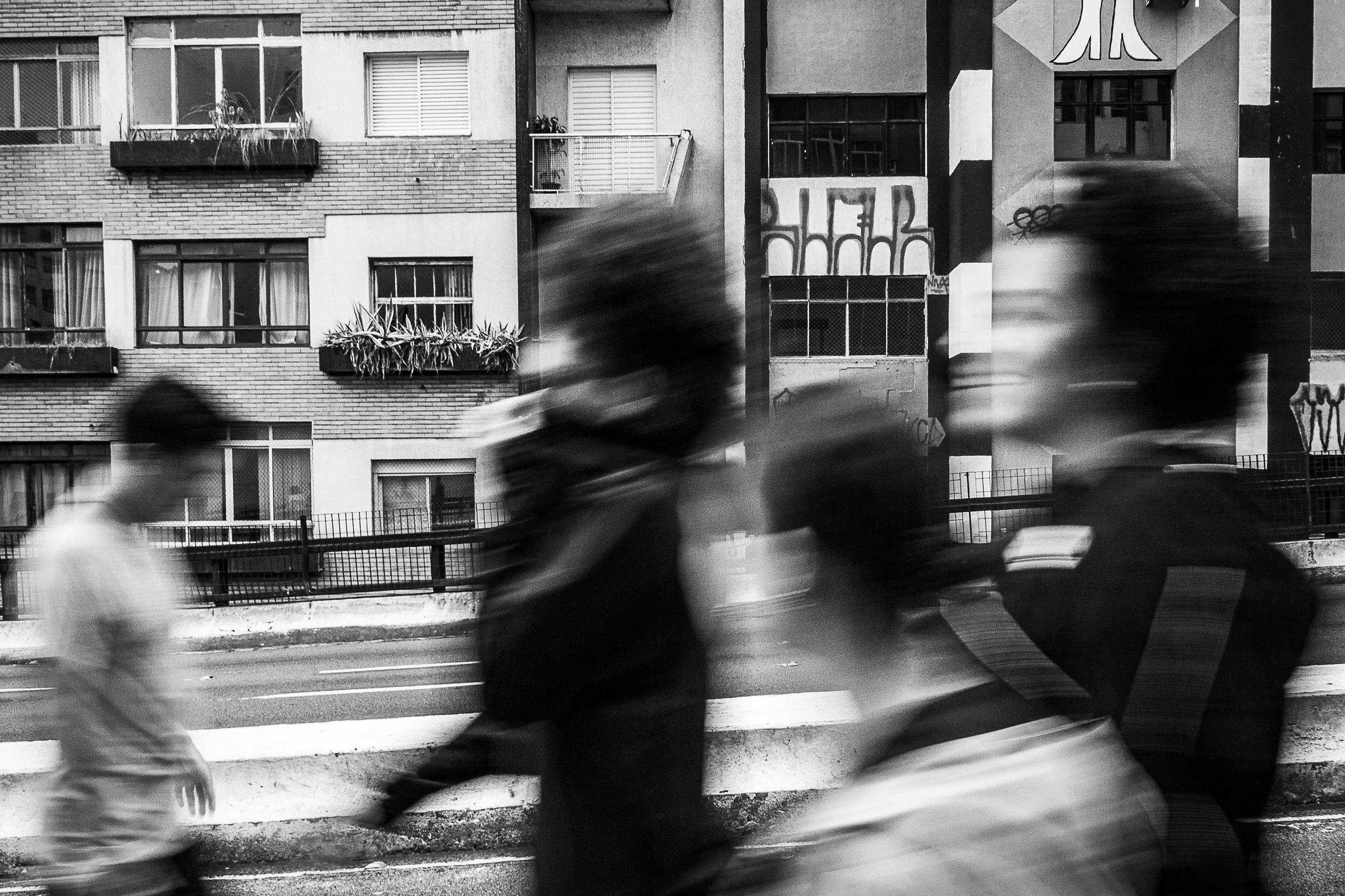 Blurred motion of people walking in front of urban buildings, creating a dynamic city scene.