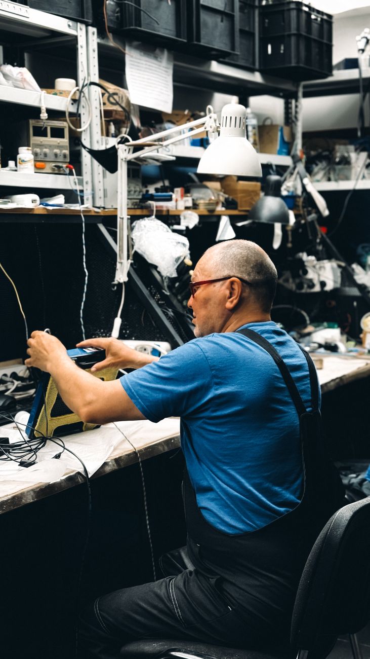 Man repairs electronics in a cluttered workshop, emphasizing dedication and skill.