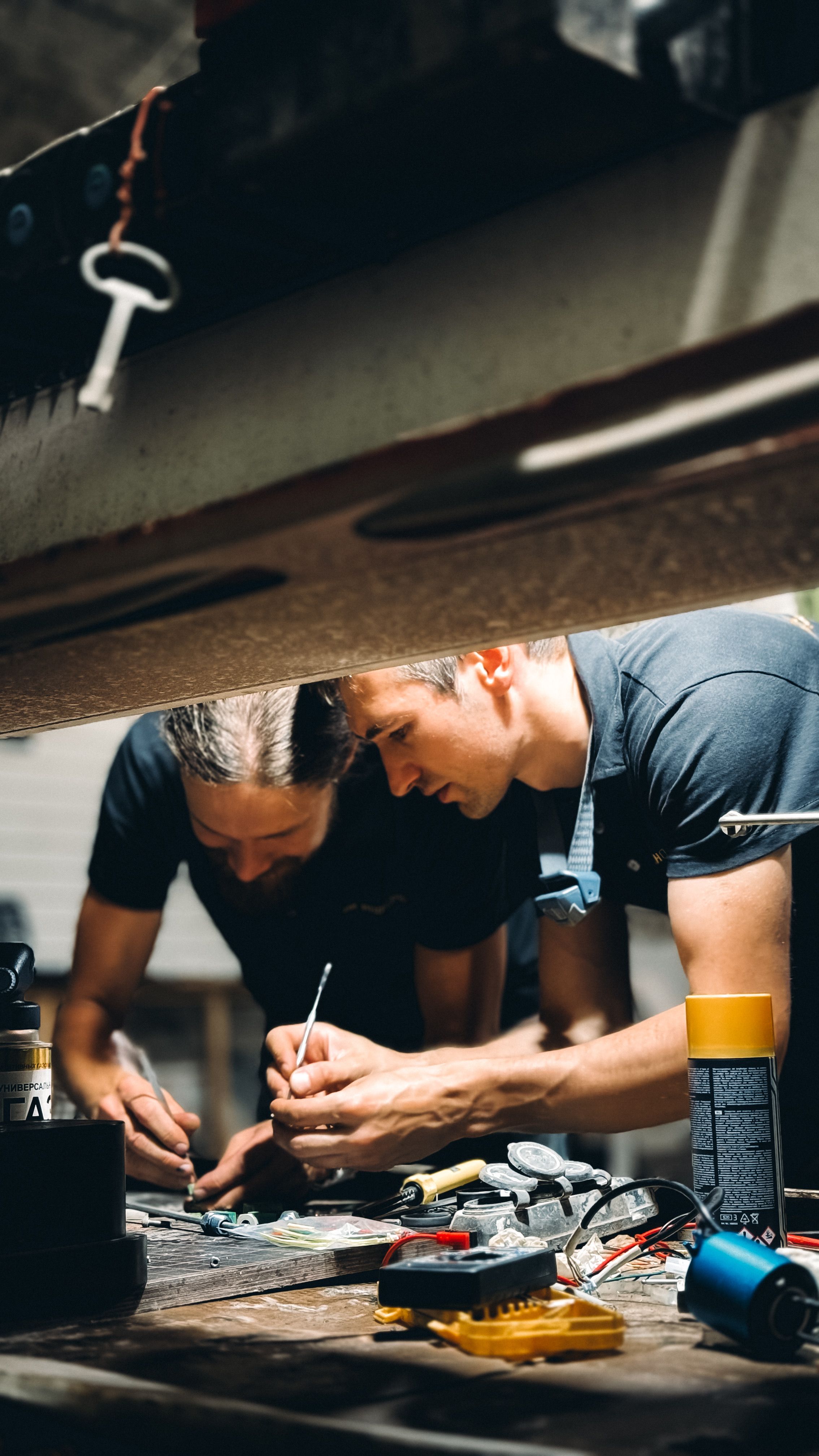 Two technicians using hand tools together while inspecting and repairing workshop machinery