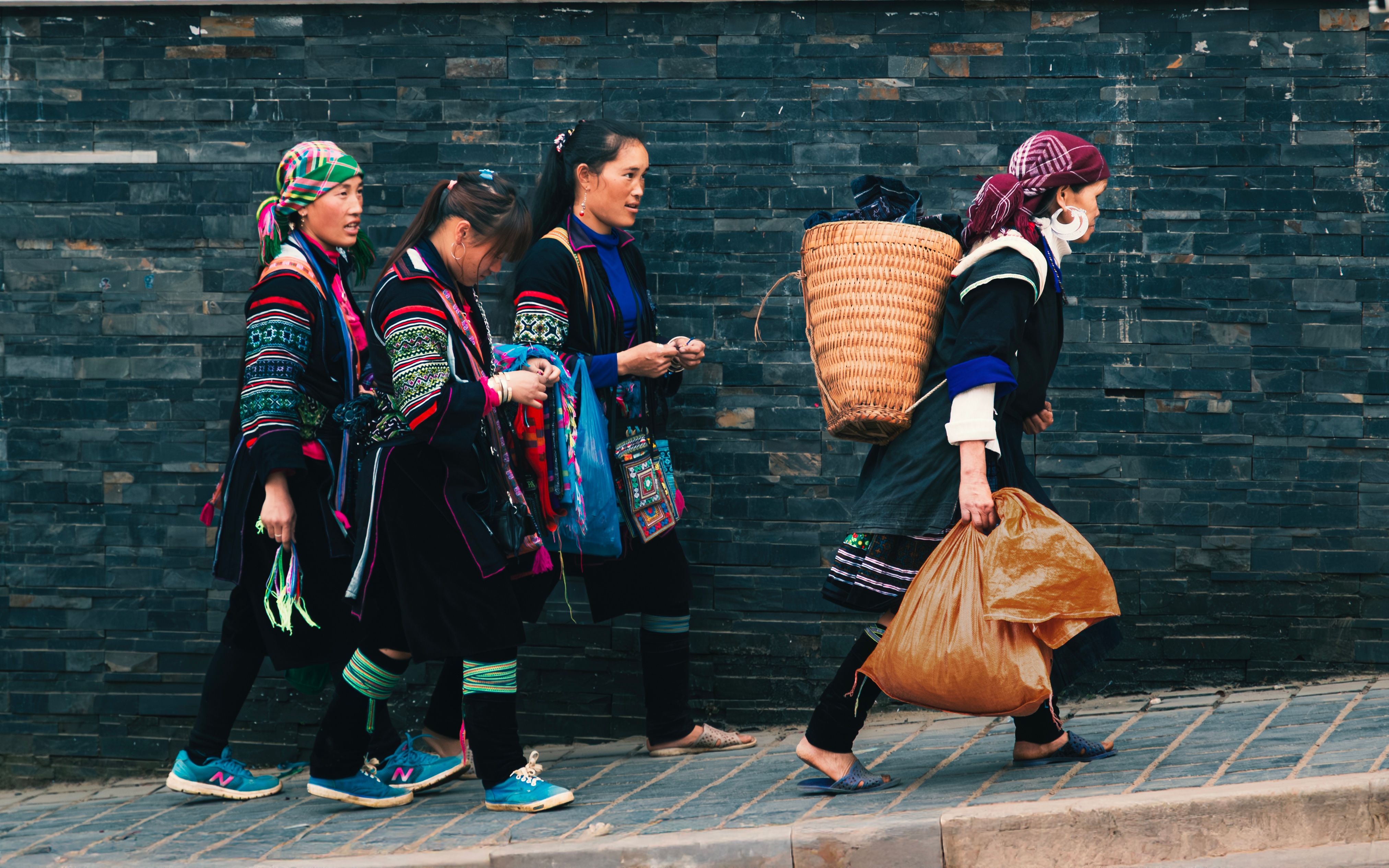 Ethnic women in traditional dress walking along a stone wall in Sapa, Vietnam.