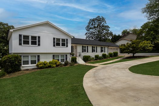 Modern suburban home with a large driveway and lush green lawn under a clear blue sky.