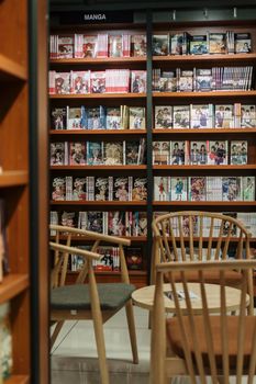 Peaceful manga bookstore section with wooden chairs and manga-filled shelves.