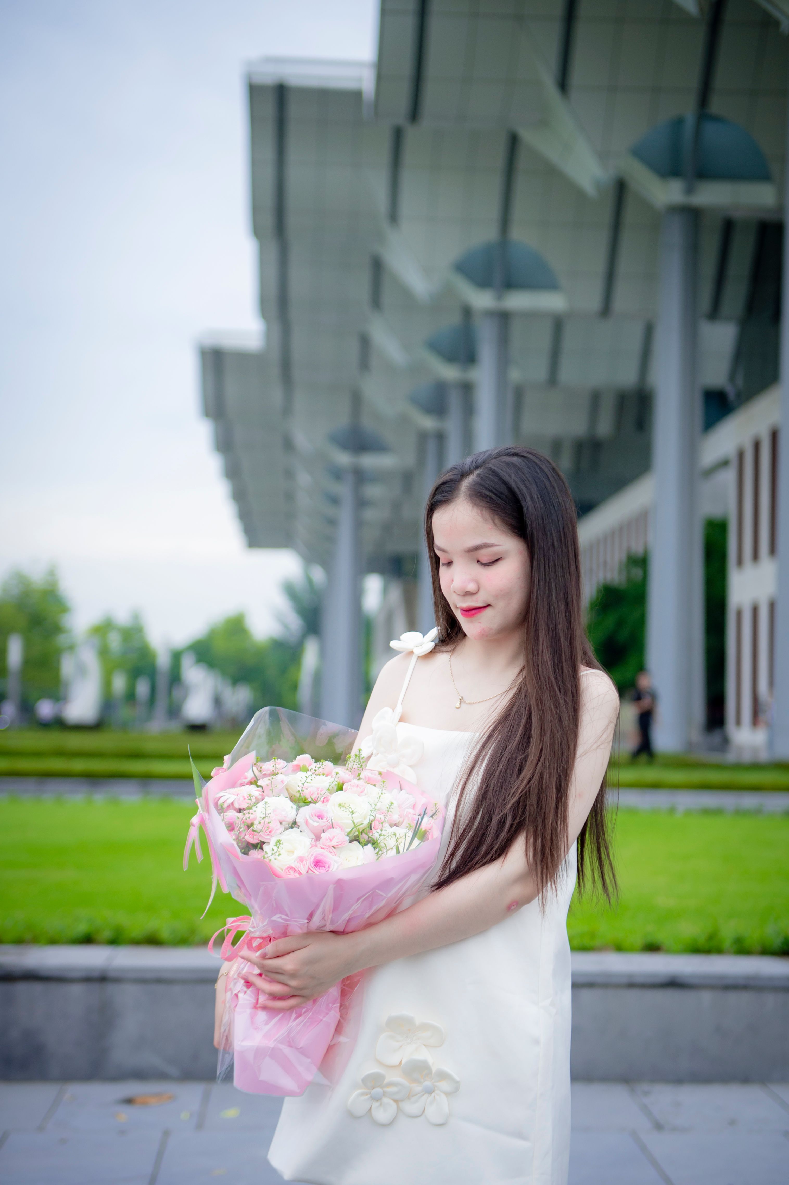 Young Woman in White Dress Holding Flowers Outdoors · Free Stock Photo