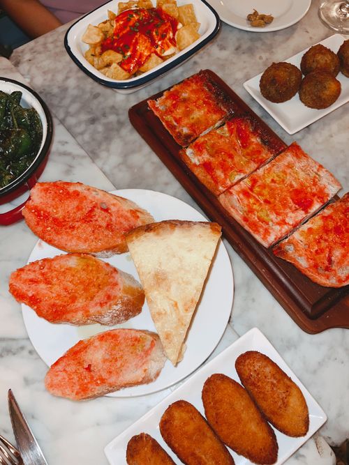 Free A vibrant spread of Spanish tapas including patatas bravas, bread with tomato, and croquettes on a marble table. Stock Photo