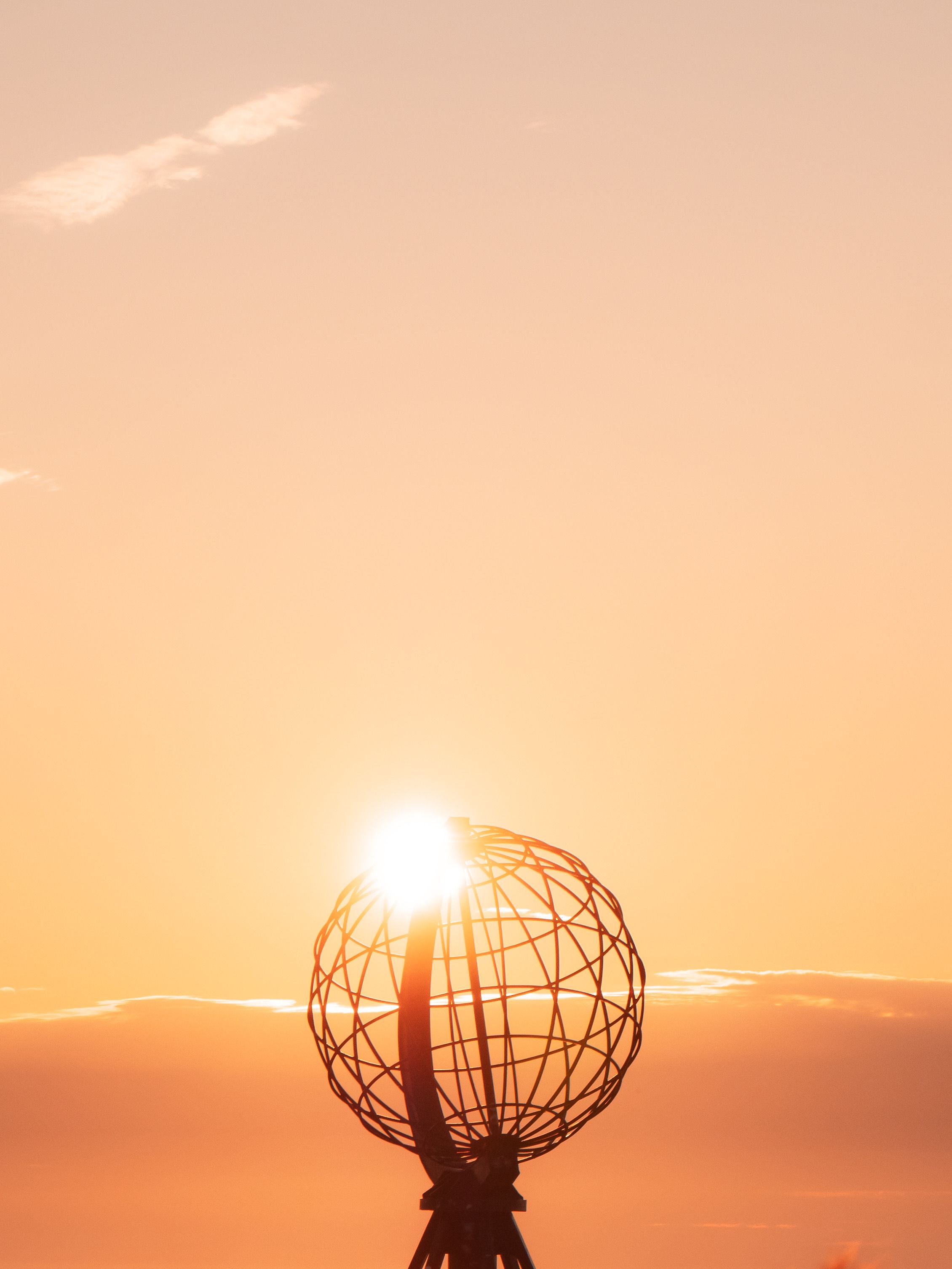 Sunset behind the globe monument at North Cape, Norway, casting a warm glow.