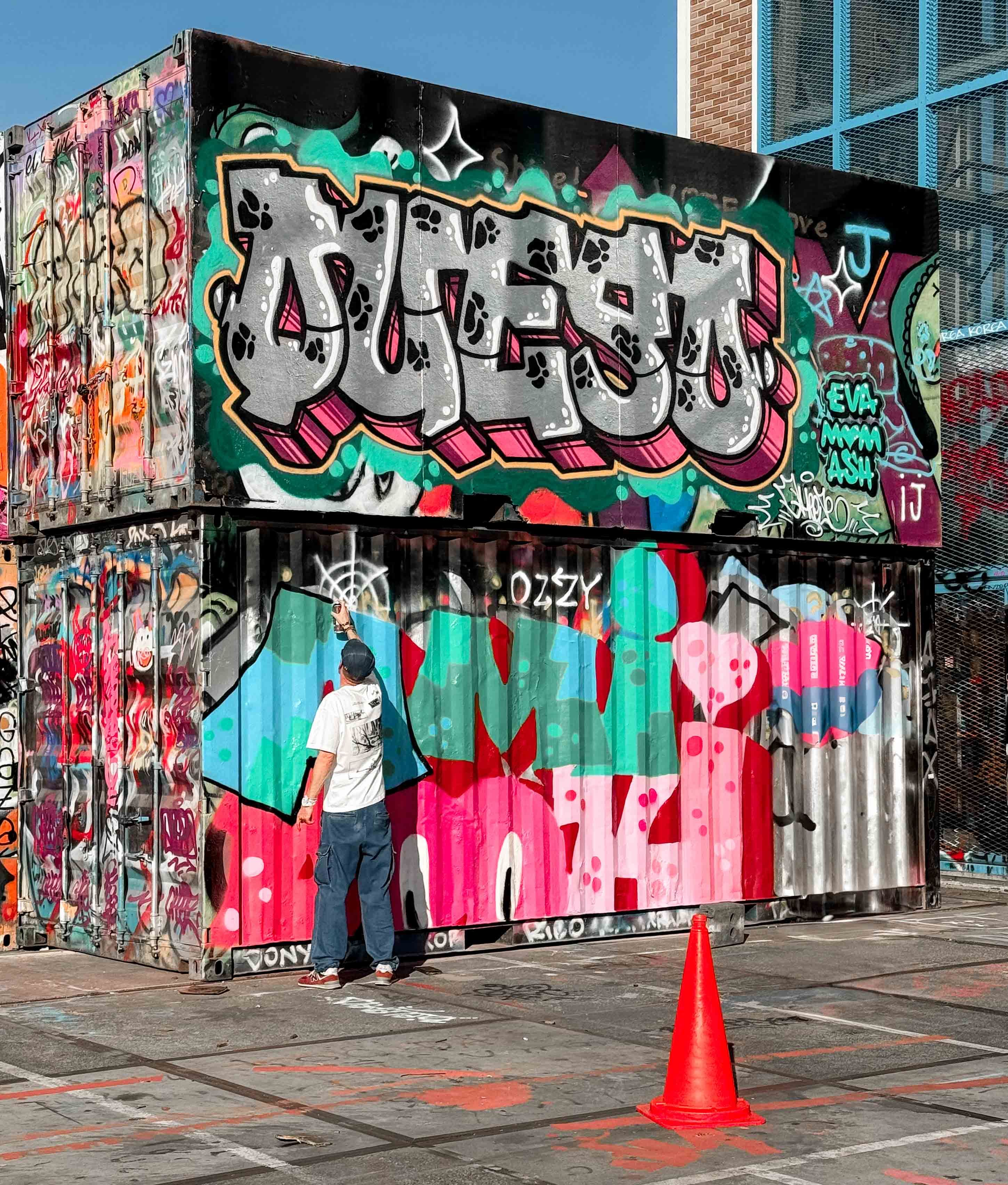 Man spray painting vibrant graffiti on stacked containers in urban area.