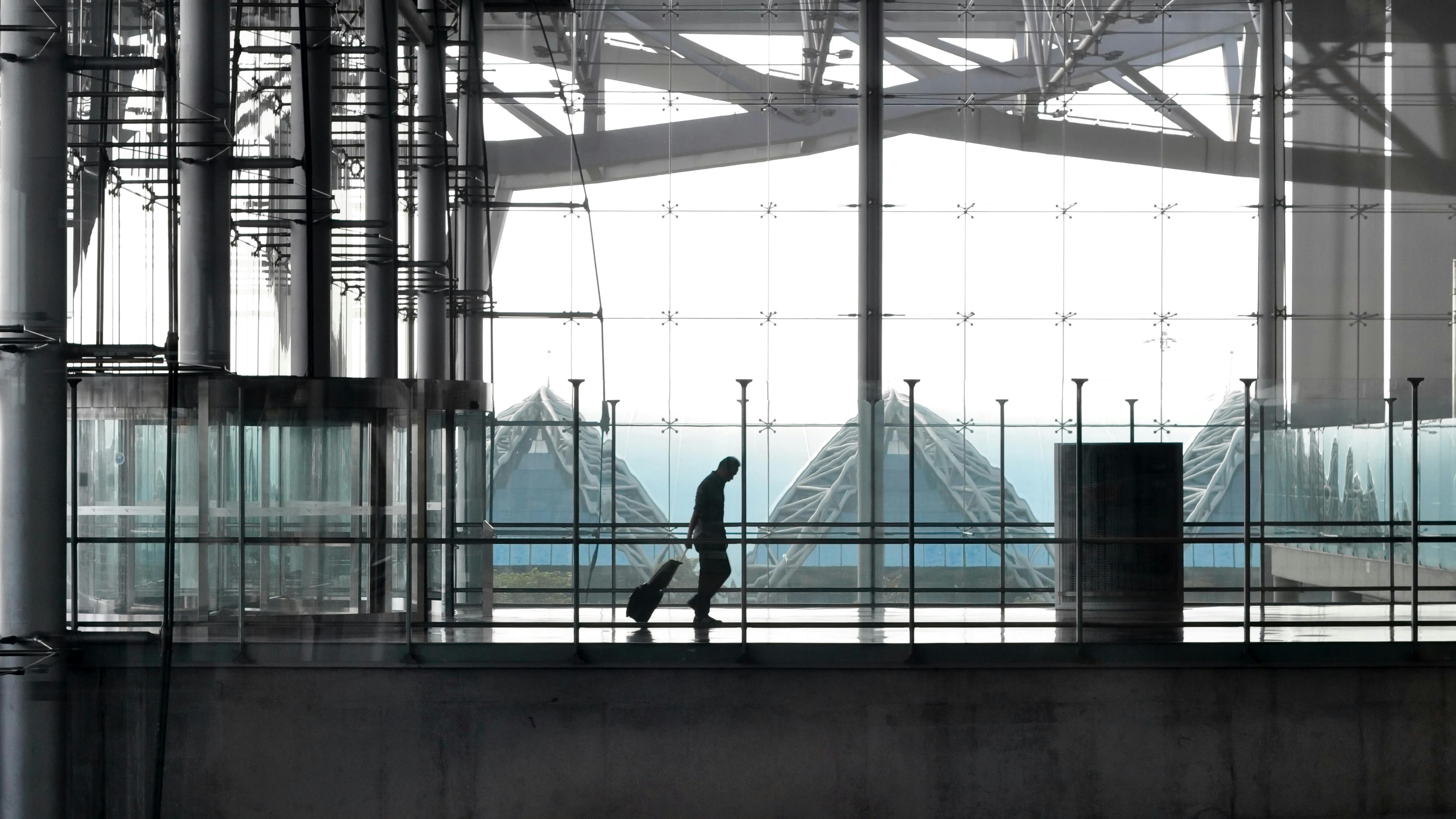 Silhouette of a traveler with suitcase in a modern glass and steel airport terminal.