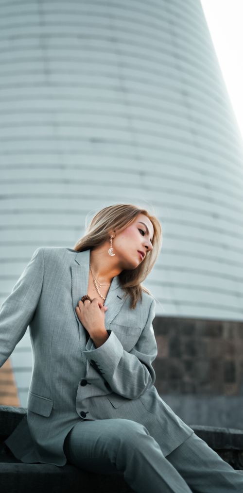 Free Confident woman posing in a grey suit against a modern architectural backdrop. Stock Photo