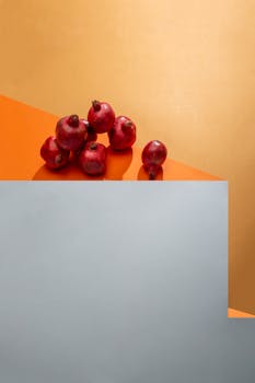 Minimalist still life featuring red pomegranates on geometric colored surfaces.