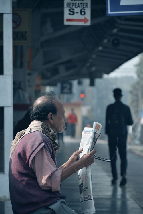 Free Elderly man reading newspaper at a Kolkata train station on a calm winter morning. Stock Photo