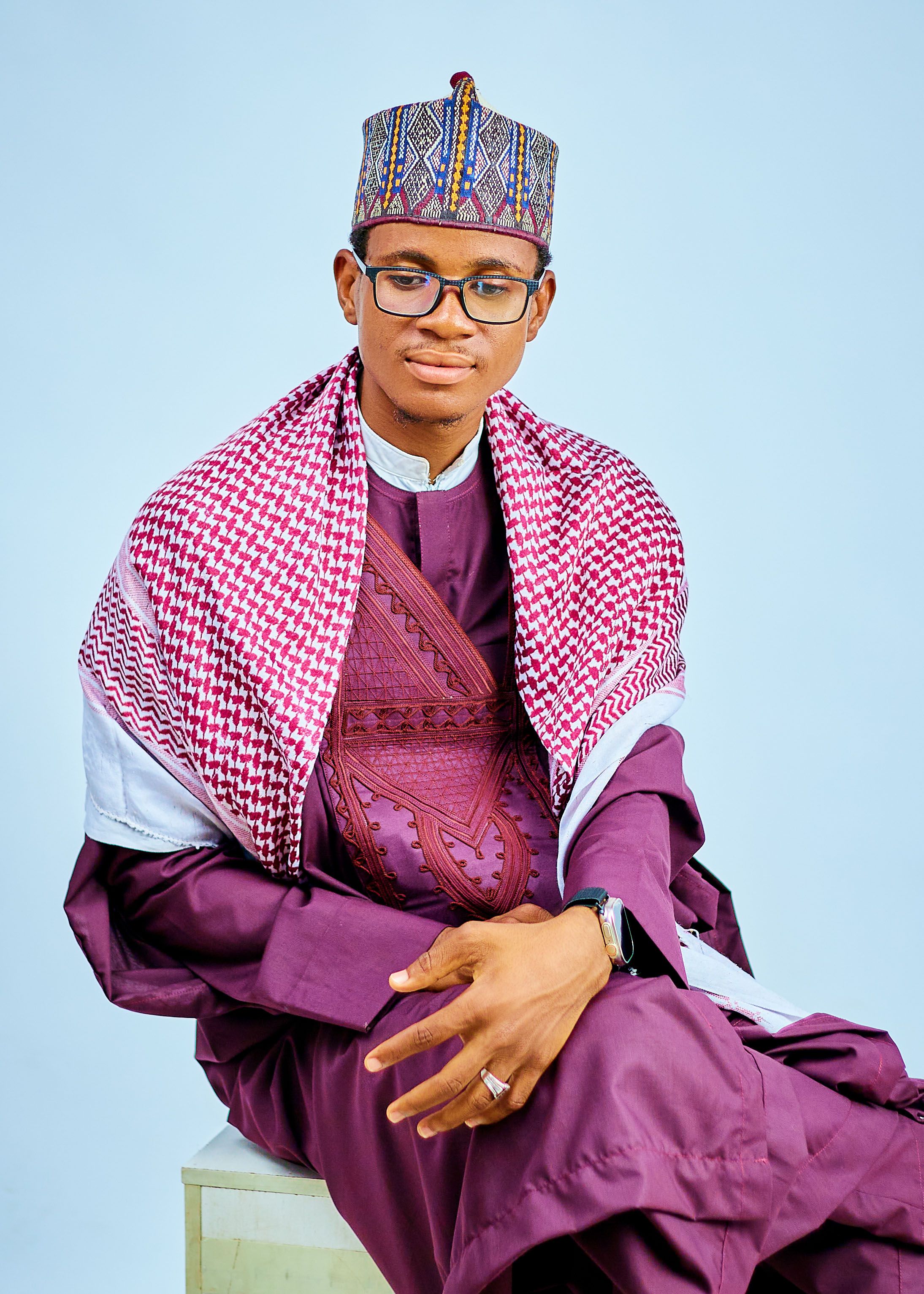 Portrait of a young man wearing traditional African attire with patterned shawl and cap.