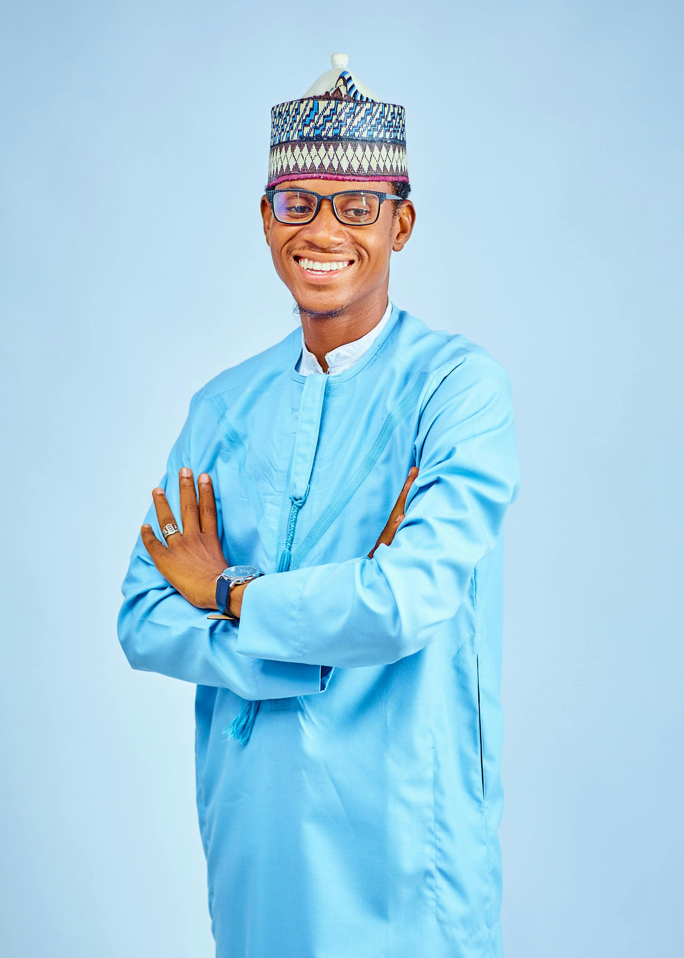 Portrait of a smiling man in traditional blue attire with arms crossed and clear background.