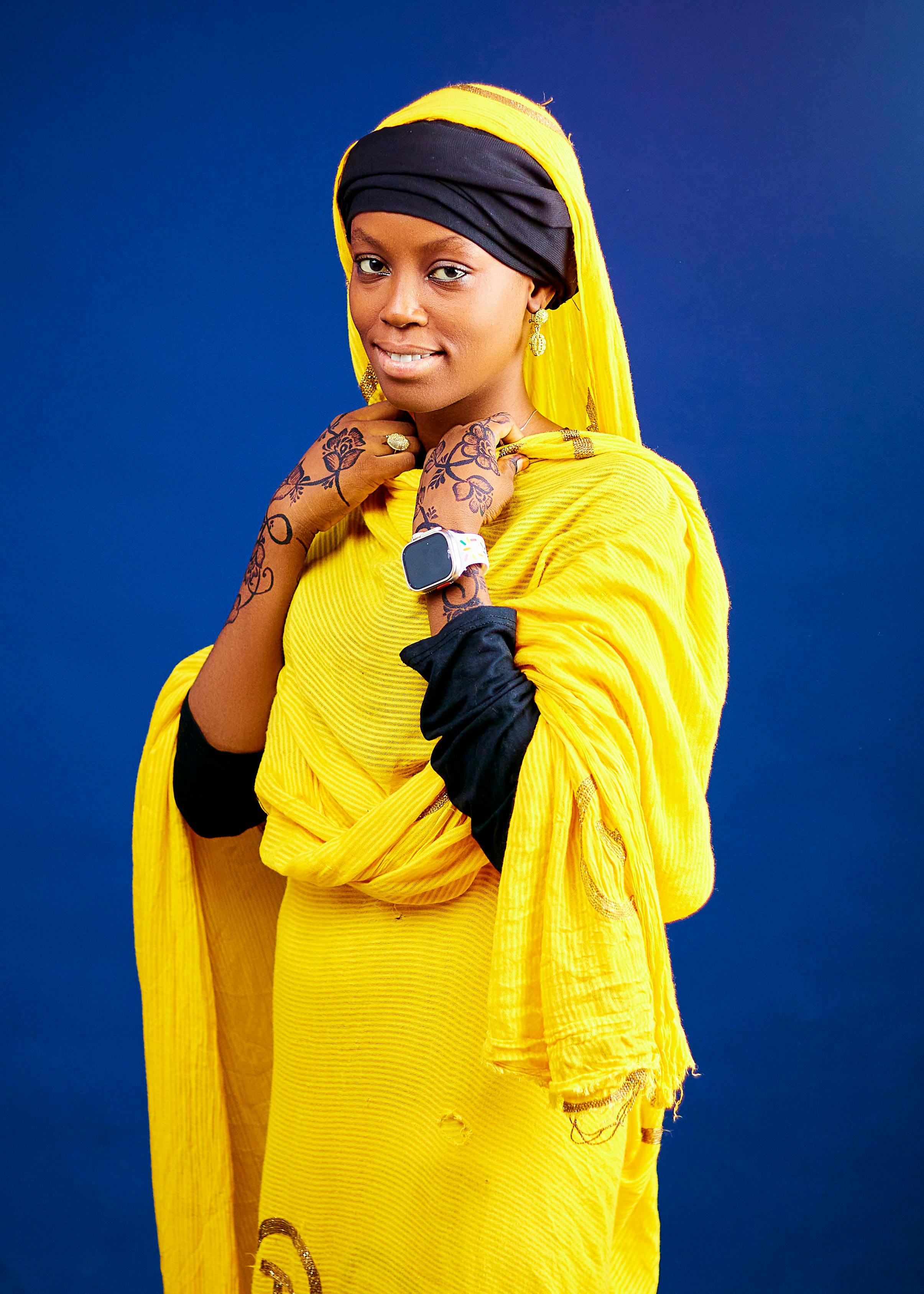 Woman in bright yellow traditional dress with henna, posing on a blue background.