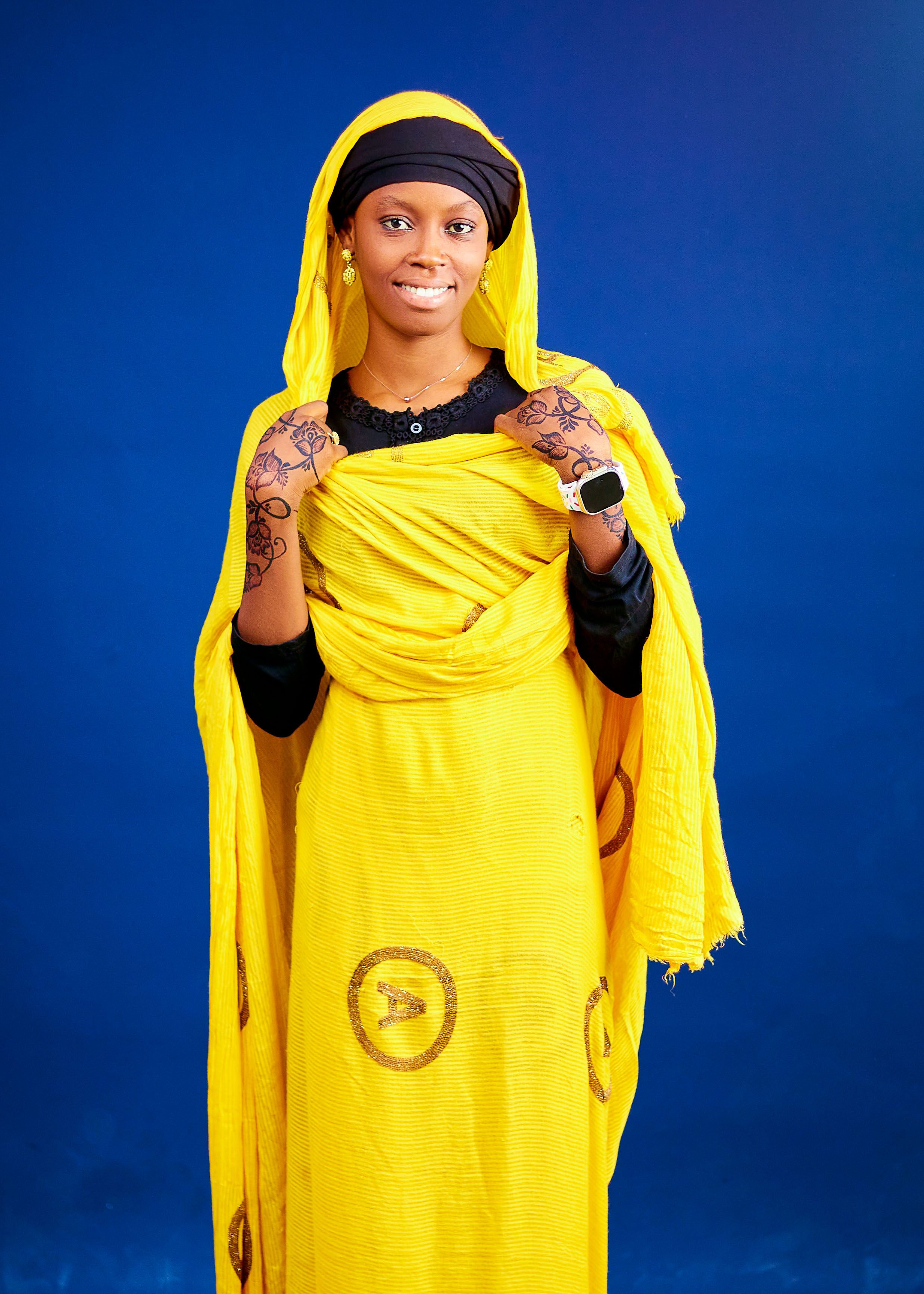Woman in vibrant yellow traditional dress against blue background, showcasing elegant style.