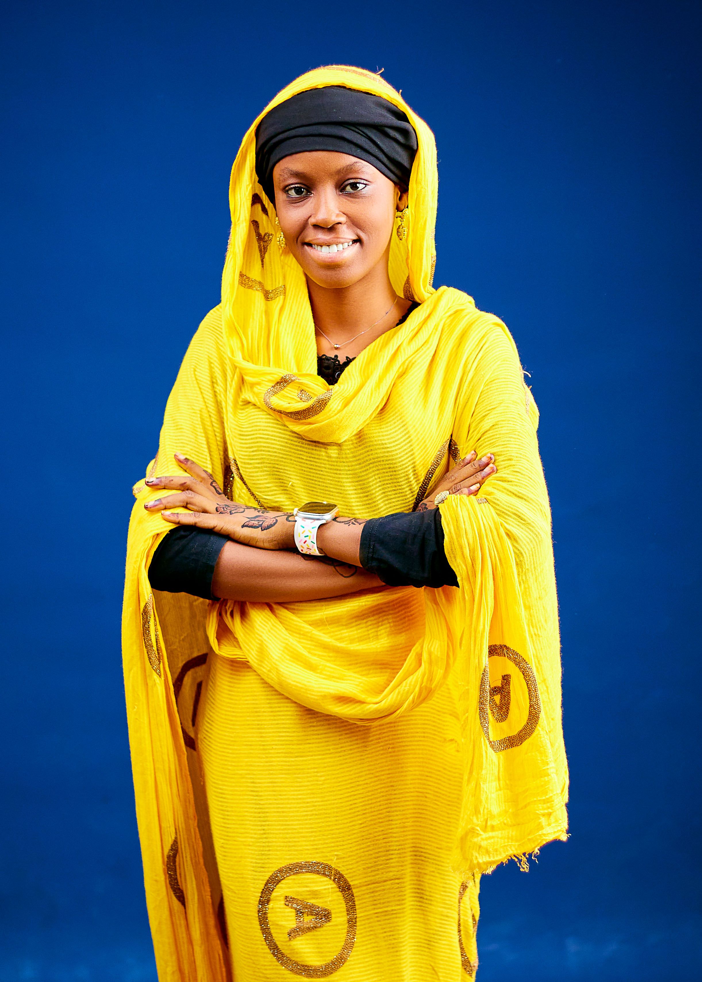 A woman in bright yellow traditional attire against a blue background, exuding confidence.