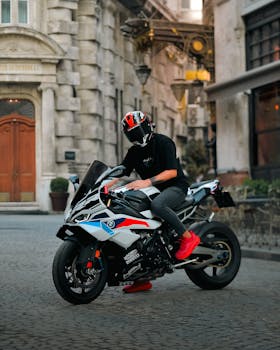 Man with helmet sits on a sleek sports motorcycle in a rustic urban setting.