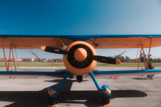 Front view of a colorful vintage biplane on an airport runway against clear blue skies.