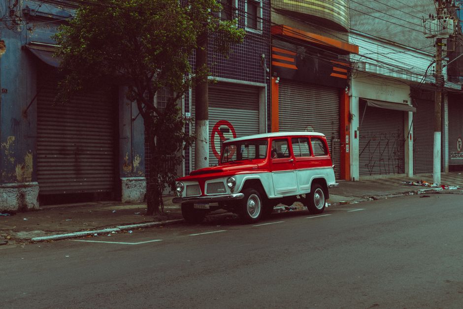 Classic red and white vintage jeep parked on an empty street with closed shops.