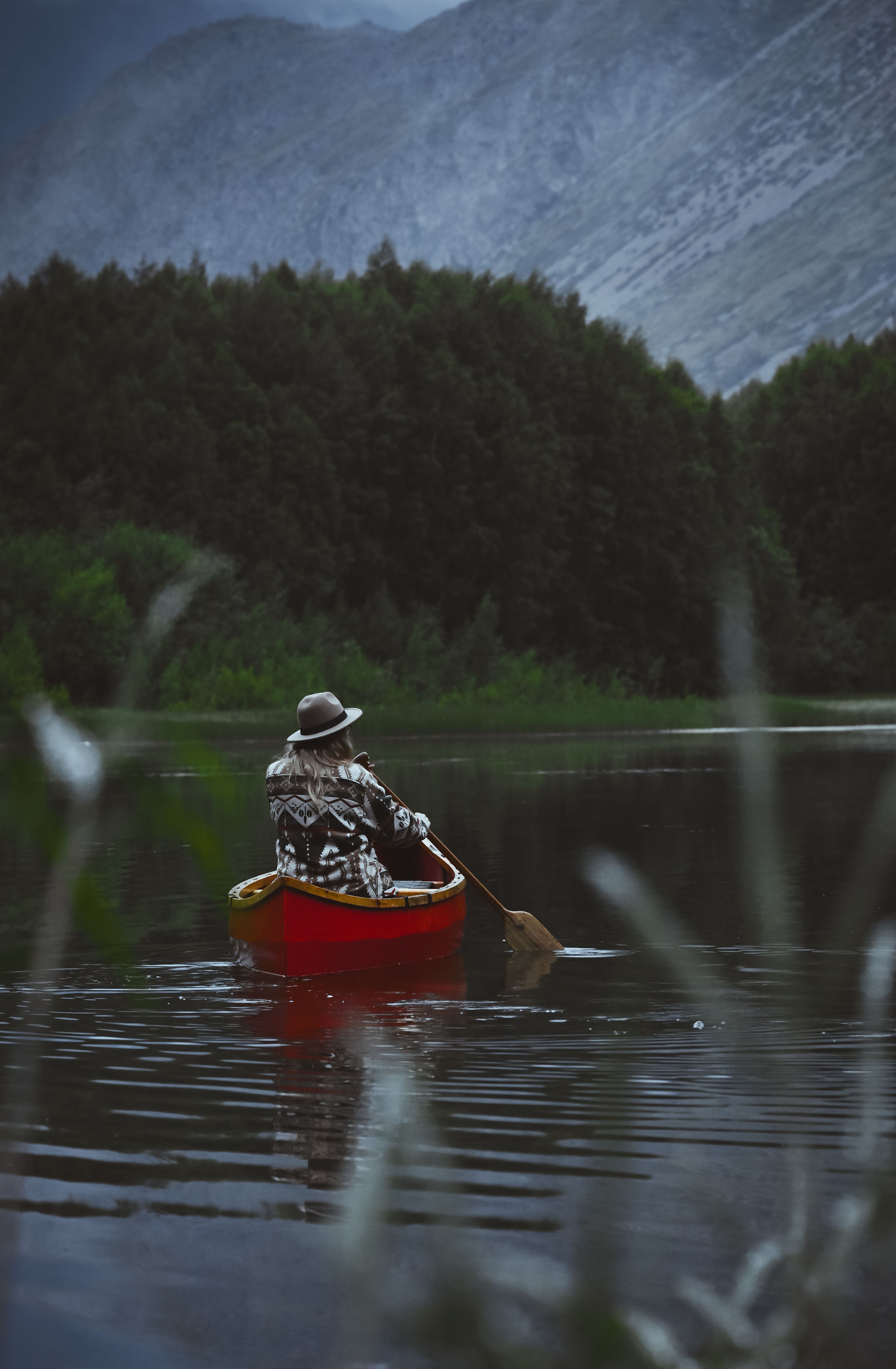 Person canoeing in a serene mountain lake surrounded by lush forest and towering peaks.