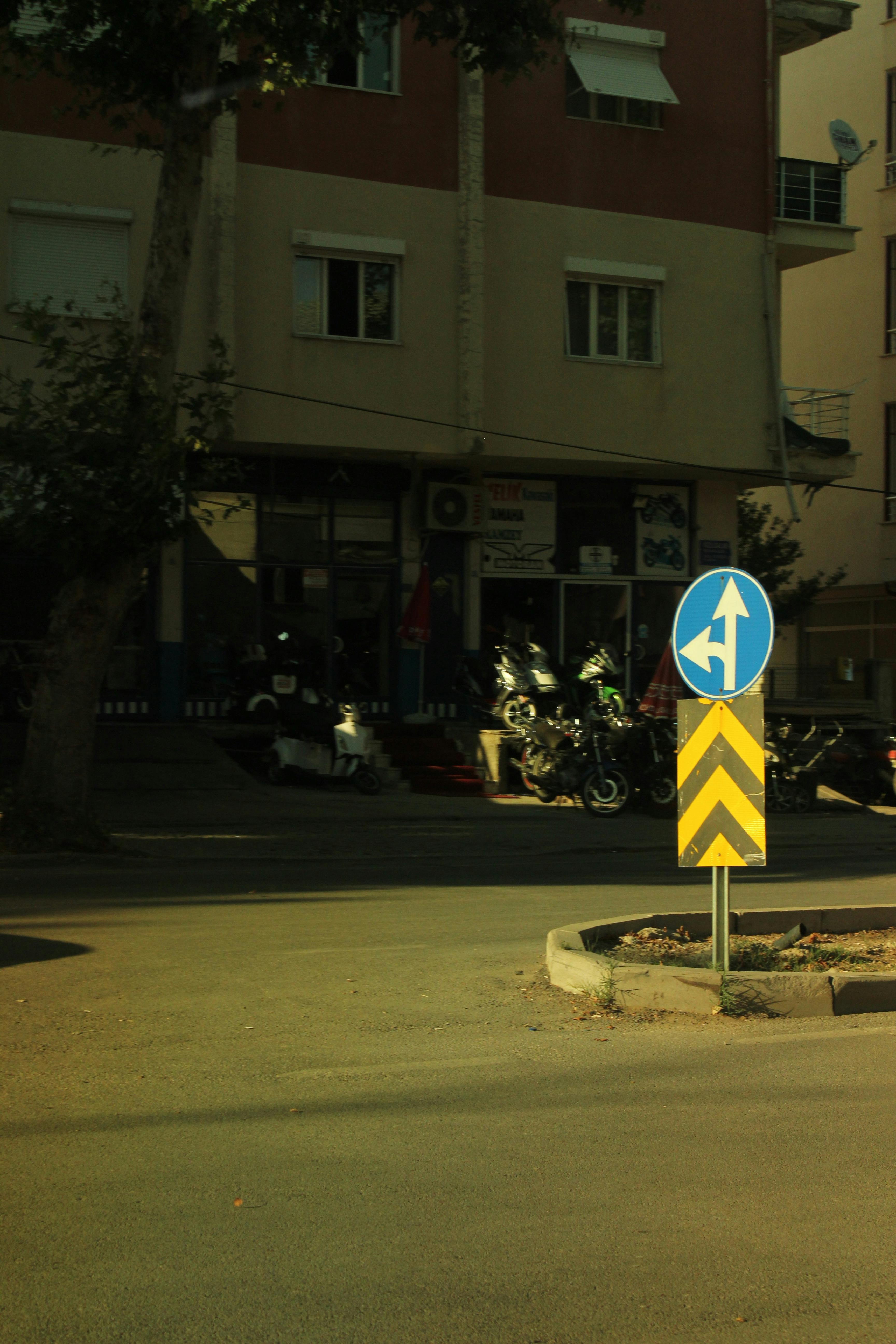 Gratuit O colț de stradă în oraș cu un indicator rutier proeminent și motociclete parcate, creând o atmosferă urbană. Fotografie de stoc