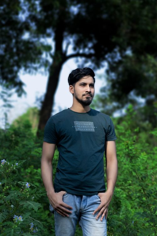 Free A young man stands confidently outdoors surrounded by greenery. Stock Photo