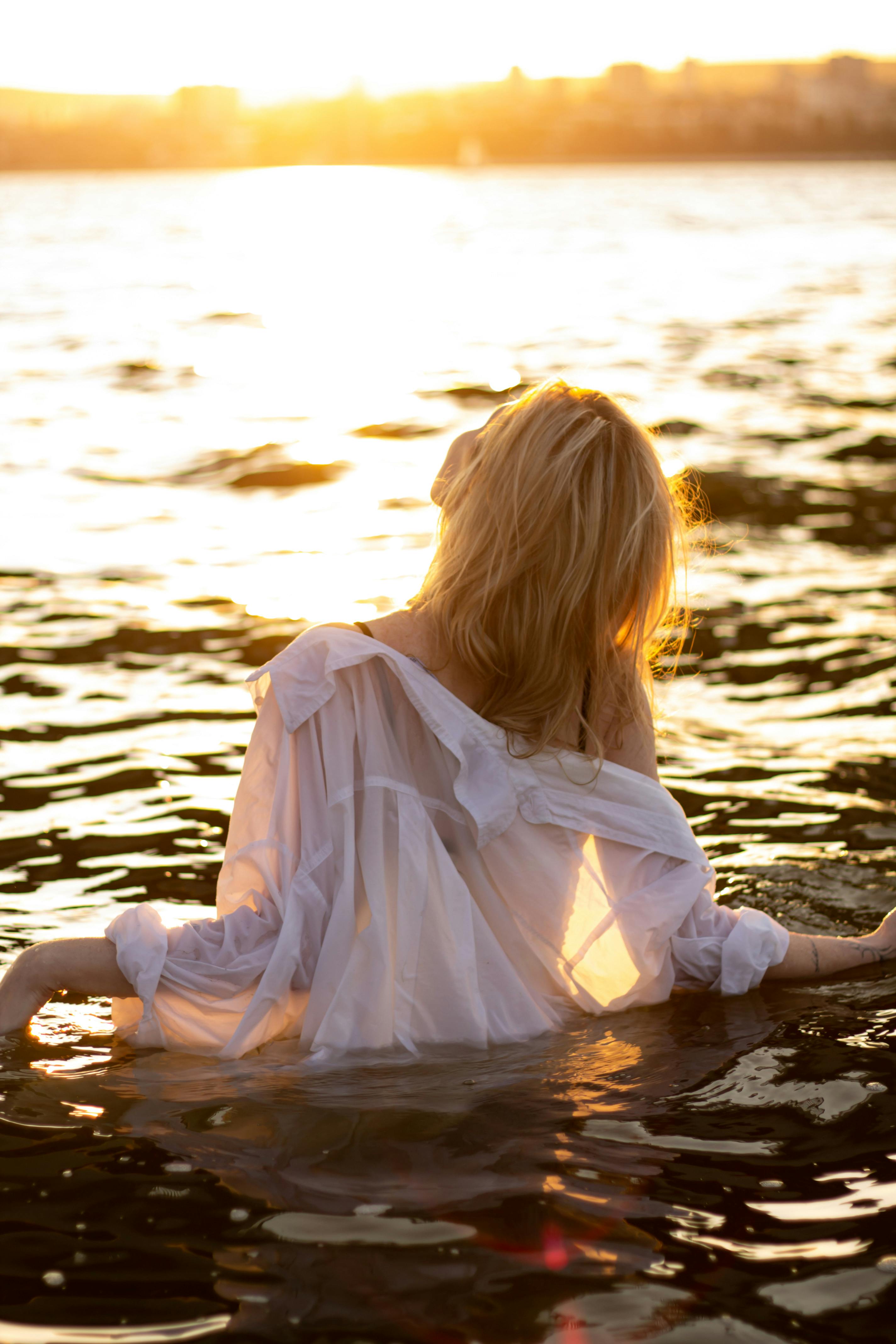A woman in a white dress stands in water at sunset in Saratov, Russia.