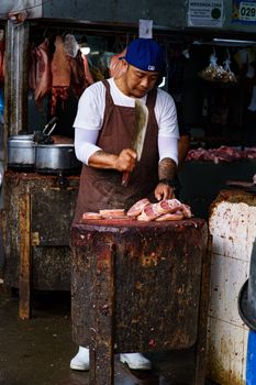 Butcher skillfully chops fresh meat at a bustling market stall, showcasing traditional techniques.