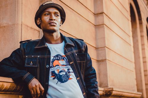 Free Stylish young man poses in denim jacket with graphic tee, creating a modern urban vibe. Stock Photo