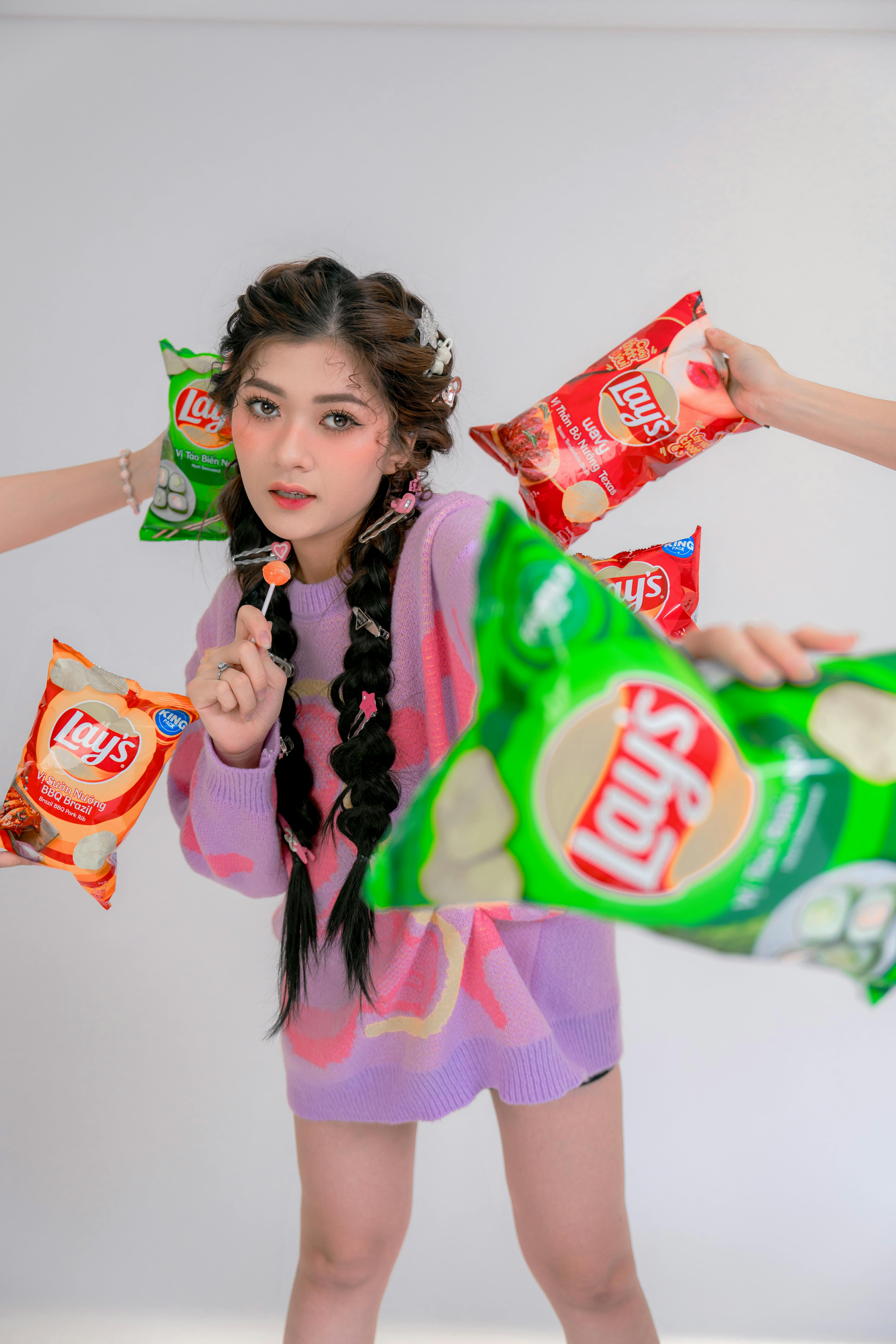 Stylish young woman surrounded by colorful chip bags indoors.